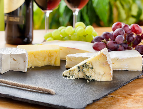 Variety of cheeses on plate next to grapes & wine