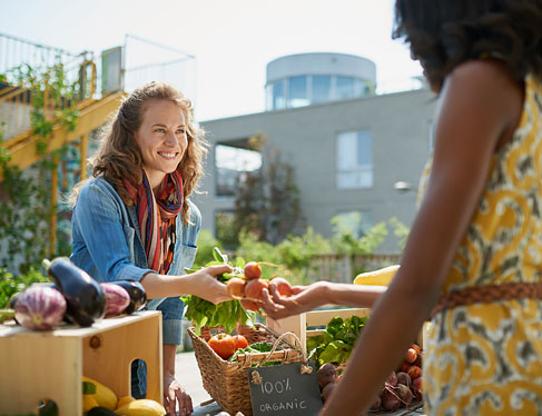 Two women handing vegetables to each other at farmers market