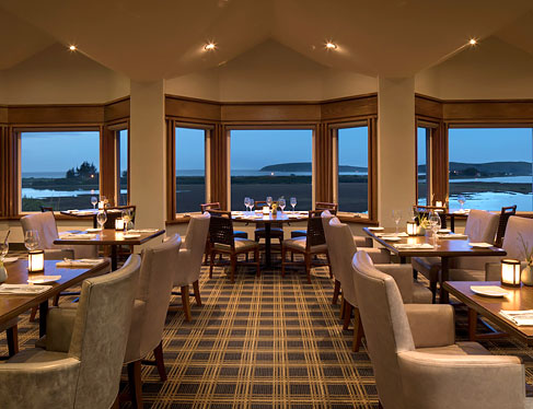 Drakes restaurant with wooden tables set for meal, sofa chairs & window panels with ocean view